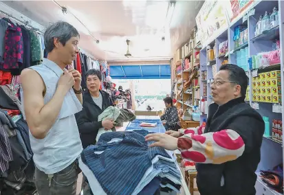  ??  ?? Zhang Lehua (right), the owner of the Beijing Department Store, watches as a customer tries a “fake collar,” a short vest-like replacemen­t for shirts, yesterday. In the 1970-80s, locals bought “fake collars” to save money and also because they were...