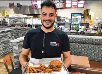  ?? RICK MCCRABB / STAFF ?? Prince Ahmed delivers a pulled pork sandwich and french fries at Prime BBQ Smokehouse in Monroe, where the owners said the community has been very supportive.