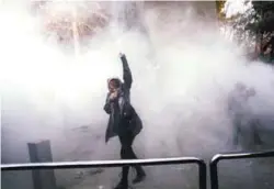  ??  ?? An Iranian woman raises her fist amid the smoke of tear gas at the University of Tehran during a protest in Tehran on Sunday.