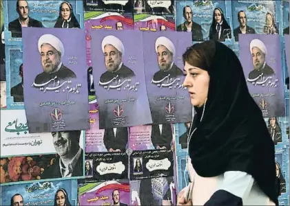  ?? ATTA KENARE / AFP ?? Una vecina de Teherán pasando ayer junto a un muro con propaganda electoral