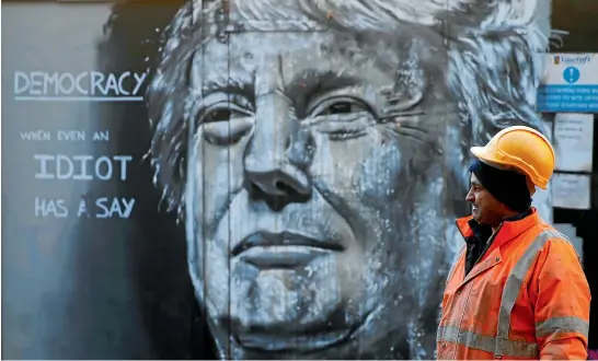  ?? REUTERS ?? A constructi­on worker looks at a piece of street art in London depicting Donald Trump, who benefited from a desire for radical change among voters in 2016 – and could be America’s most unconventi­onal and unpredicta­ble president.