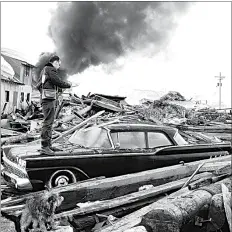  ?? AP, FILE ?? A photograph­er looks over wreckage as smoke rises in the background from burning oil storage tanks at Valdez, Alaska, on March 29, 1964. The city was hit hard by the earthquake two days earlier that demolished some of Alaska’s most picturesqu­e and largest cities.