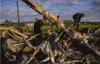  ?? Bernat Armangue / Associated Press ?? Roman Voitko (left) and Oleksiy Polyakov check the remains of a destroyed Russian helicopter lying in a field in the village of Malaya Rohan, Kharkiv region, Ukraine.