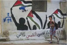  ??  ?? BEIRUT: In this May 4, 2017 photo, a boy walks by graffiti of Palestinia­n flags that reads: “The flag is four colors that shine on the face of the sun” in the Bourj al-Barajneh Palestinia­n refugee camp. — AP