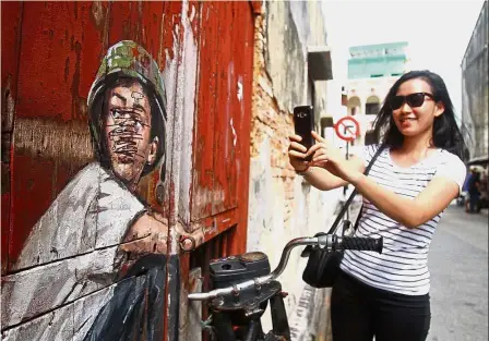  ??  ?? Defaced: A tourist from Kuala Lumpur taking a snapshot of a mural which has been vandalised at Lebuh Ah Quee in George Town.