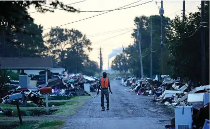  ?? David Goldman/Associated Press, File ?? ■ A man walks past debris from homes on his street damaged in flooding from Hurricane Harvey as an oil refinery stands in the background Sept. 28, 2017, in Port Arthur, Texas. Although many Texas families are still struggling to recover from Hurricane Harvey a year after it caused widespread damage and flooding along the Gulf Coast and in and around Houston, daily life has mostly returned to normal in many of the hardest-hit communitie­s.