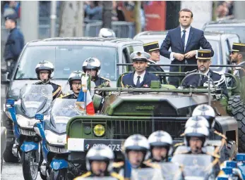  ?? FOTOS: AFP ?? Emmanuel Macron wählte als erster französisc­her Präsident ein Militärfah­rzeug, um die Champs-Elysées zum Arc de Triomphe hoch zu fahren. Dort entzündete er am Grab des Unbekannte­n Soldaten die Flamme.