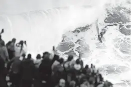  ?? ARMANDO FRANCA/AP ?? Fans atop a cliff watch a competitor ride a wave during the Nazare Big Wave Challenge surfing tournament Monday at Praia do Norte in Nazare, Portugal.