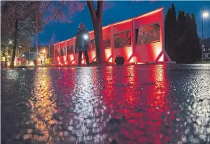  ?? JENS MEYER THE ASSOCIATED PRESS ?? A woman walks beside an illuminate­d fence, an art installati­on showing the former border demarcatio­n, prior to the 30th anniversar­y of the falling of the Berlin Wall.