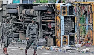  ?? | AFP ?? SECURITY personnel walk past a burned vehicle along a road after they were torched by protesters in Colombo, yesterday amid protests over the country’s economic crisis.