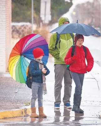  ?? MARLA BROSE/JOURNAL ?? Israel McMullin and his sons, Atticus, 6, left, and Sebastian, 10, pause in the rain at a Northeast Heights intersecti­on while on their way to school Wednesday. The rain broke a city dry spell that extended to 96 days, the fifth-longest such period on...