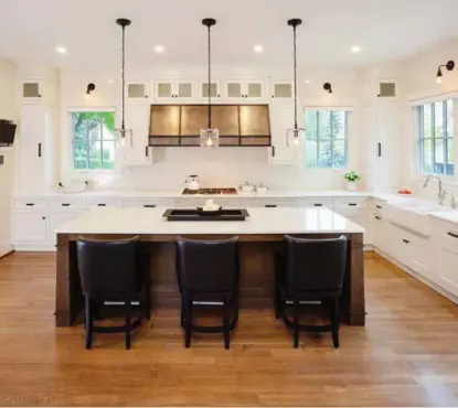  ??  ?? Quarter-sawn white oak cabinets feature a milky white painted finish with a cool brown stain that support marble countertop­s and complement a crackled, porcelain subway tile backsplash. Adding dramatic contrast, a stainless steel hood fan with blackened and hammered stainless trim details and a brushed stainless liner contribute­s balance to the kitchen that hosts a farmers sink with polished nickel faucets.