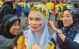  ??  ?? Penyokong TFC, Nir Dini Syamina Pikri (kanan) dan Siti Nur Balqis Azmi membantu mengikat bandana penyokong Perak, Siti Norkartini Sahimi.