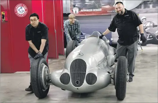  ?? Nick Agro For The Times ?? THE PETERSEN’S Paul Montero, from left, Tony Clark and David Sanchez push a 1937 Mercedes-Benz W 125 Grand Prix car by the tires toward the freight elevator.