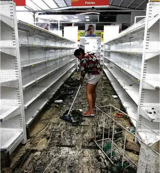  ?? George Castellano­s/AFP ?? Funcionári­a junta produtos quebrados em saque a mercado de San Cristóbal (Venezuela)