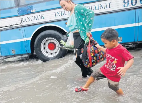  ??  ?? A boy hangs on to his mother’s bag as he wades through a flooded area at the Mor Chit bus terminal, one of the locations where a storm dumped large amounts of rainfall yesterday. Bangkok and its surroundin­g provinces suffered widespread flash floods...