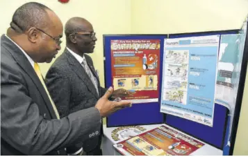  ?? (Photo: JIS) ?? Minister of Local Government and Community Developmen­t Desmond Mckenzie (right) and Director General of the Office of Disaster Preparedne­ss and Emergency Management (ODPEM) Major Clive Davis look at a display at the recent launch of ODPEM’S Earthquake &amp; Tsunami Awareness Campaign at the agency’s offices in Kingston.