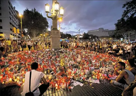  ?? Emilio Morenatti/Associated Press ?? People stand next to candles and flowers placed on the ground Sunday in Barcelona, Spain, after terror attacks in the region of Catalonia that killed at least 14 people and wounded over 120.