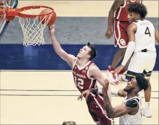  ?? Kathy Batten / Associated Press ?? Oklahoma guard Austin Reaves shoots past West Virginia forward Derek Culver during the second half on Saturday. Reaves had 28 points in the double-ot win.