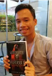  ?? — Nicole Renee David ?? ALEGA AND HIS BOOK. University of the Assumption architectu­re student and author Xavier Efraem Alega smiles as he holds his book The Labyrinth of Minerva V.