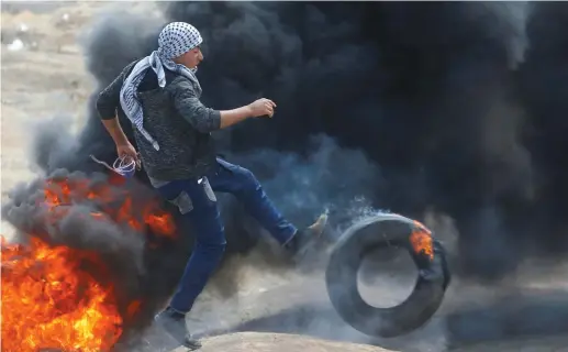  ?? (Mohammed Salem/Reuters) ?? A PALESTINIA­N kicks a burning tire at the Israel-Gaza border Monday. ‘Images create a partial reality, ignoring the reality outside the focused frame as well as the wider context.’