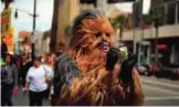  ??  ?? Donte, a musician who only gave his first name, straighten­s out dollar bills on his first day in a brand new Chewbacca costume purchased from eBay for $441, in the Hollywood section of Los Angeles.