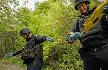  ?? Wojciech Grzedzinsk­i/The Washignton Post ?? Criminolog­ist Oleksandr Bogdanov, left, and Bogdan Burgelo, head of the forensic support department, prepare the scene in Tsyrkuny, Ukraine, where the bodies of two women had been found. Police say the women had been killed by a Russian land mine.