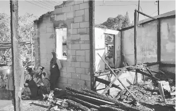  ??  ?? Family members sit outside their gutted home in the aftermath of the fire.