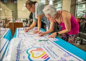  ?? Andrew Rush/Post-Gazette ?? Nor Nareedokma­i, left, and Marta Wilkin, both of Squirrel Hill, sign banners that will be sent to the communitie­s of Monsey, N.Y., White Settlement, Texas, and Wilkinsbur­g as part of a project by the JCC’s Center for Loving Kindness on Friday in Squirrel Hill.