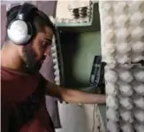  ??  ?? Syrian rapper Amir al-Muarri works with earphones on, in front of his microphone-equipped booth, padded with soft foam and egg cartons, in his room.