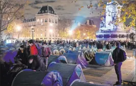  ?? Alexandra Henry The Associated Press ?? Migrants set up a makeshift camp Monday night on Place de la Republique in Paris. Paris police are under government orders to explain themselves after officers were filmed tossing migrants out of tents while evacuating a camp in the French capital.