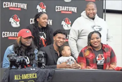  ?? Jeremy Stewart ?? Cedartown football player CJ Washington (seated, center) celebrates signing his National Letter of Intent to play for the University of Georgia with his family during a special ceremony in the HON Room at the Polk County College and Career Academy on Wednesday, Dec. 15. With him are his sister Zykeria Washingto (seated, from left), his son Grayson Washington, his mother Brittany Hammock, his sister Jamaria Washington (standing from left) and his stepfather Corey Hammock.