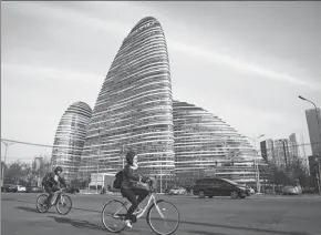  ?? IMAGES QILAI SHEN / BLOOMBERG VIA GETTY ?? Cyclists ride past commercial buildings of a SOHO project in Beijing.