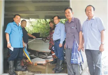  ??  ?? Jamit (third right) and others look at the damage to Kaya’s house. Kaya estimates his loss due to the landslide at RM15,000.