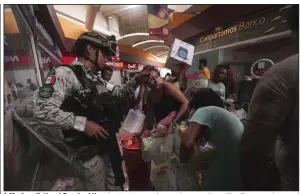  ?? (AP/Marco Ugarte) ?? A Mexican National Guard soldier tries to stop people carrying away items like diapers and canned goods Wednesday, while others take electronic­s from a store at a shopping mall after Hurricane Otis ripped through Acapulco, Mexico.