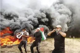  ??  ?? GETTING BLOODIER – Palestinia­n protesters cover their faces as they chant slogans next to burning tires during clashes with Israeli troops along Gaza’s border with Israel, April 6. (AP)