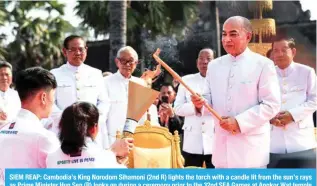 ?? ?? SIEM REAP: Cambodia’s King Norodom Sihamoni (2nd R) lights the torch with a candle lit from the sun’s rays as Prime Minister Hun Sen (R) looks on during a ceremony prior to the 32nd SEA Games at Angkor Wat temple in Siem Reap province on March 21, 2023. – AFP