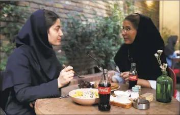  ?? Associated Press ?? Two Iranians enjoy their time while two CocaCola bottles stand on their table at a cafe in downtown Tehran on Wednesday. Whether at upscale restaurant­s or corner stores, American brands like CocaCola and Pepsi can be seen throughout Iran despite the heightened tensions between the two countries. U.S. sanctions have taken a heavy toll, but Western food, movies, music and clothing are still widely available.
