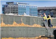  ?? THE ASSOCIATED PRESS ?? Workers stand on a flood wall made of Hesco barriers on the bank of the Cedar River in Cedar Rapids, Iowa.