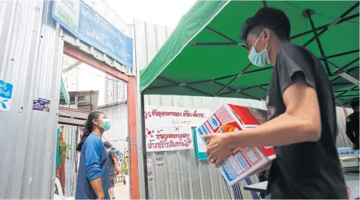  ?? WICHAN CHAROENKIA­TPAKUL ?? Workers at a constructi­on site on Soi Phetchabur­i 7 in Bangkok’s Phaya Thai district emerge to pick up delivered food. Constructi­on sites in Bangkok and its vicinity have been closed for one month following the government’s semi-lockdown imposed last Thursday.