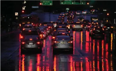  ?? (AP/Damian Dovarganes) ?? Car lights are reflected in the wet street as commuters line up to enter the I-110 Harbor freeway in downtown Los Angeles during rain earlier this month.