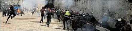  ?? Picture: REUTERS/ AMMAR AWAD ?? PANDEMONIU­M: A camera operator falls as an Israeli police officer runs after him and Palestinia­ns run away as Israeli police fire a stun grenade during clashes at the compound that houses Al-aqsa Mosque in Jerusalem's Old City.