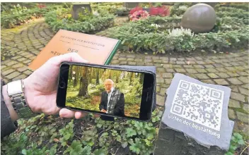  ?? FOTO: DPA ?? Ein Mann hält auf einem Friedhof in Bergisch Gladbach ein Mobiltelef­on, auf dem ein Video abgespielt wird. Auf dem Friedhof erklären mit dem Mobiltelef­on lesbare QR-Codes die Grabstätte­n und Anlagen.