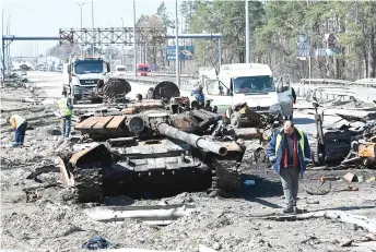  ?? — AFP photo ?? Road service workers clean debris around a burnt Russian military invasion launched on Ukraine. tank and vehicle on a road west of Kyiv during Russia’s