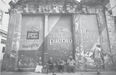  ?? RAMON ESPINOSA/AP 2020 ?? Cuba is implementi­ng deep financial reform in hopes of stemming an economic crisis and reconfigur­e a system that will still grant some universal benefits, including free health care. Above, people sit against a wall with political slogans in Havana.