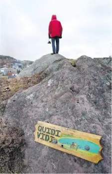  ??  ?? A man climbs rocks overlookin­g Quidi Vidi, which offers a taste of village life with a bustling city nearby.