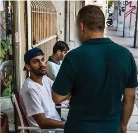  ?? FOTO: AFSHIN ISMAELI ?? En av menneskesm­uglerne snakker med migranter på en kafé i Athen.