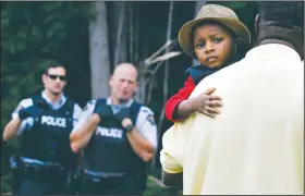  ?? AP/CHARLES KRUPA ?? A Haitian boy holds onto his father Monday as they approach an illegal crossing point, staffed by Royal Canadian Mounted Police officers, from Champlain, N.Y., to Saint-Bernard-de-Lacolle, Quebec.
