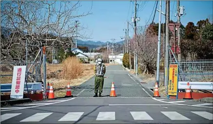  ??  ?? Un garde à l’entrée d’une zone évacuée, à Okuma, dans la préfecture de Fukushima au Japon, le 4 mars.