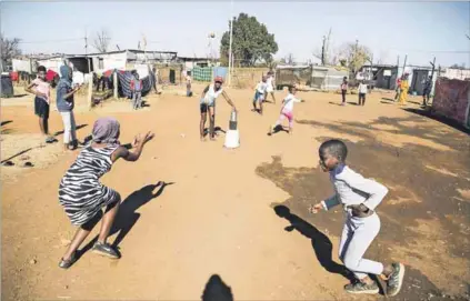  ??  ?? Life goes on: Children in Snake Park play ‘three toti’ with a can and ball. Parents in the settlement worry about the coronaviru­s, especially because many children have illnesses caused by the mine. Photos: Delwyn Verasamy